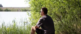 Mies istuu kivellä järven rannalla ja katselee järvelle.