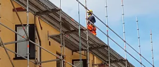 Työmies rakennustelineillä talon katolla.