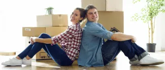Pariskunta istuu lattialla muuttolaatikoiden edessä.