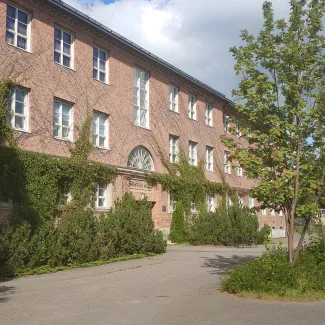 Punatiilinen rakennus, jonka seinustalla köynnöskasveja. Etualalla pihlaja punaisine marjoineen