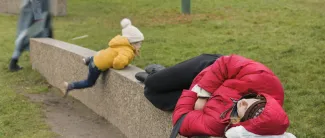 Nainen nukkuu kiviaidalla ja pieni lapsi kiipeää aidan yli.