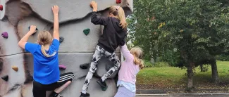 Kolme tyttöä kiipeilee liikennepuiston seinäkiipeilyseinällä.