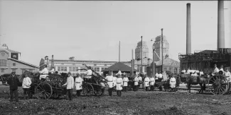 Varkauden tehtaiden palokunta valkoisine palokuntapaitoineen poseeraa ryhmäkuvassa kaluston kanssa Varkauden tehtaiden edustalla