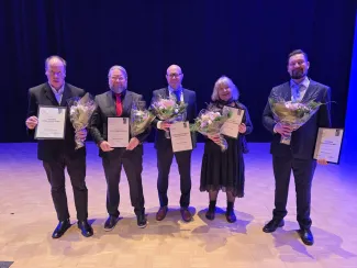 Viisi ihmistä rivissä kunniakirjojen ja kukkien kanssa.